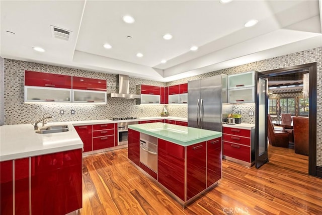 kitchen featuring a center island, wall chimney range hood, appliances with stainless steel finishes, tasteful backsplash, and wood-type flooring