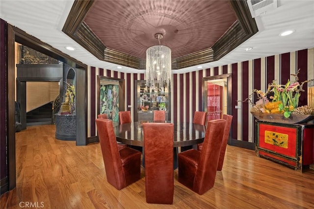 dining space with a chandelier, light wood-type flooring, and a raised ceiling