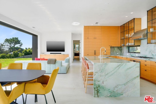 kitchen with sink, wall chimney range hood, a kitchen breakfast bar, backsplash, and stainless steel gas stovetop