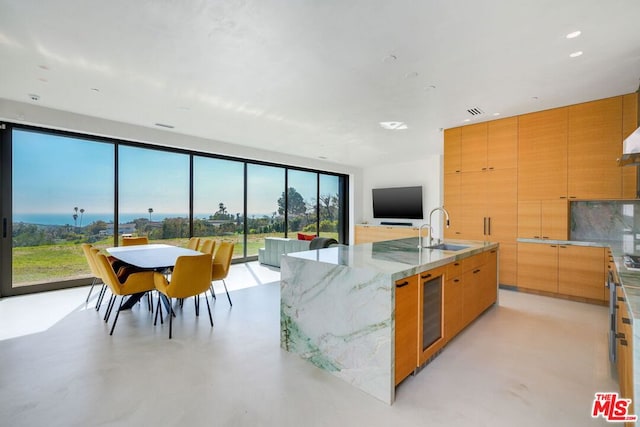 kitchen with light stone counters, wine cooler, a spacious island, and sink