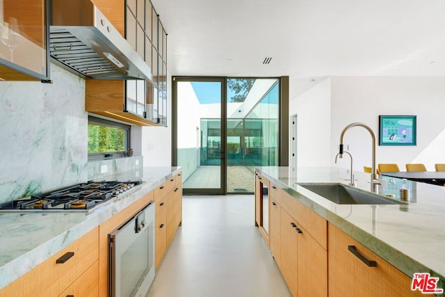 kitchen featuring stainless steel gas stovetop, light stone counters, sink, and range hood