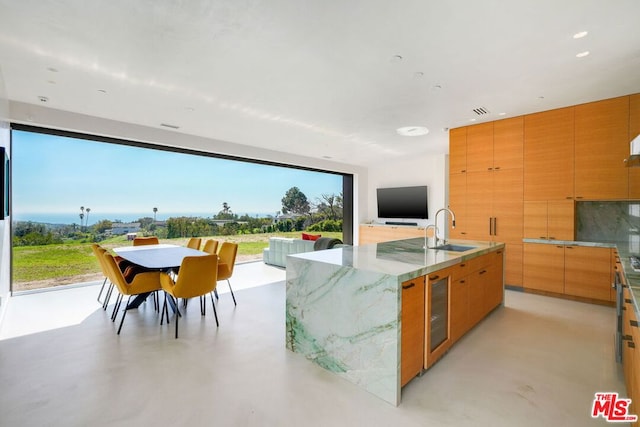 kitchen featuring a large island, light stone countertops, sink, and beverage cooler