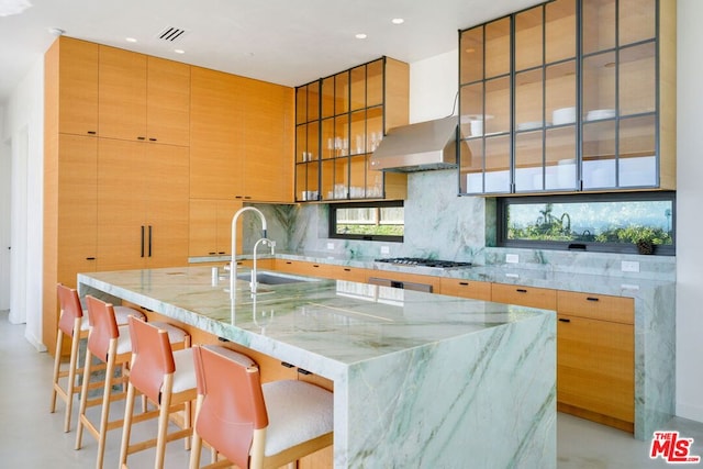 kitchen with a kitchen bar, decorative backsplash, light stone counters, stainless steel gas cooktop, and a spacious island