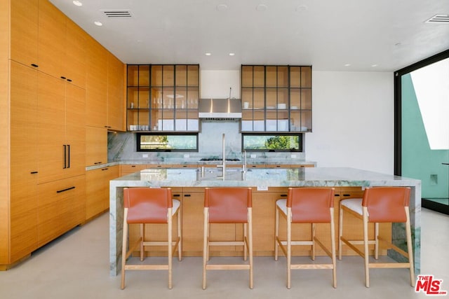 kitchen featuring a breakfast bar area, tasteful backsplash, a large island, and wall chimney range hood