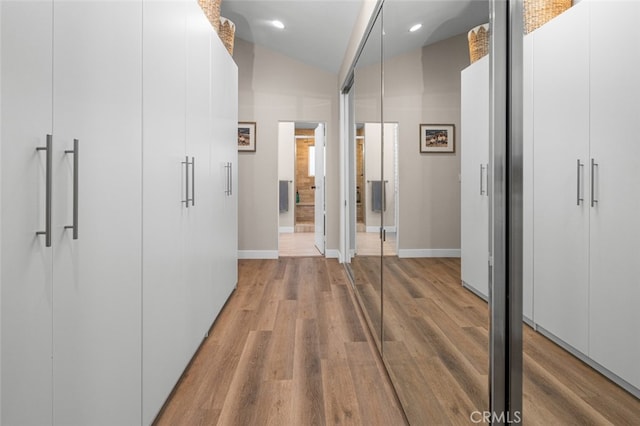 corridor with hardwood / wood-style floors and vaulted ceiling