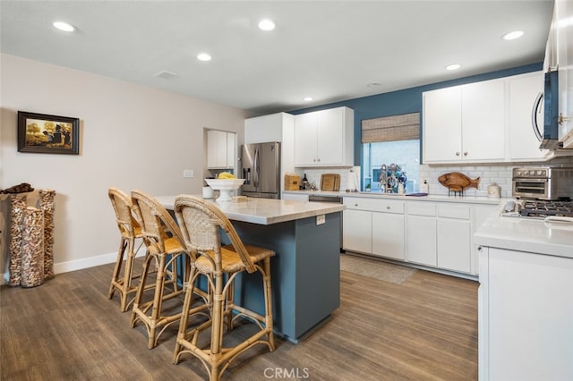 kitchen with appliances with stainless steel finishes, a center island, white cabinetry, and hardwood / wood-style floors