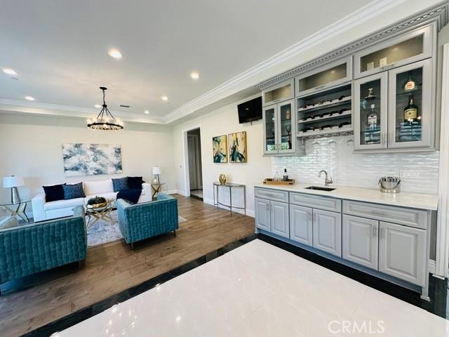 bar with dark hardwood / wood-style flooring, tasteful backsplash, gray cabinetry, sink, and decorative light fixtures