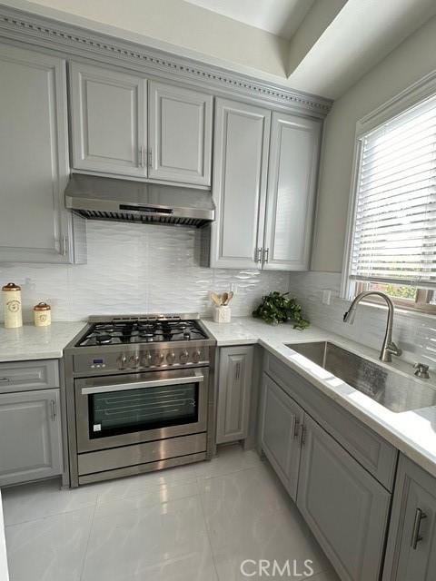 kitchen with high end stove, backsplash, gray cabinetry, and sink