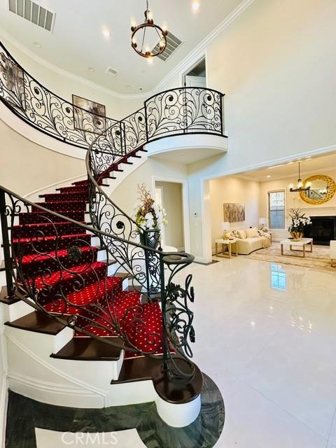 stairway featuring a fireplace, a high ceiling, ornamental molding, and a notable chandelier