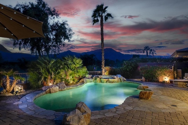 pool at dusk featuring an in ground hot tub, a mountain view, and a patio area