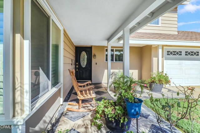property entrance featuring a shingled roof, covered porch, and stucco siding