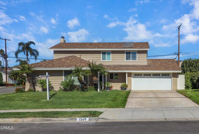 traditional-style home with a garage, a front lawn, a chimney, roof mounted solar panels, and driveway