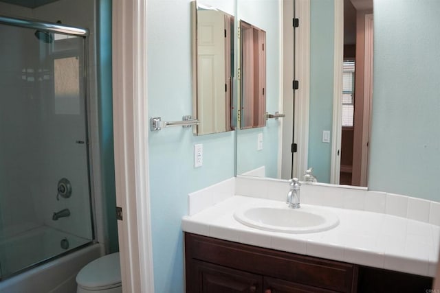 full bathroom with combined bath / shower with glass door, vanity, and toilet