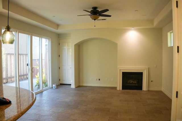 unfurnished living room featuring a raised ceiling and ceiling fan