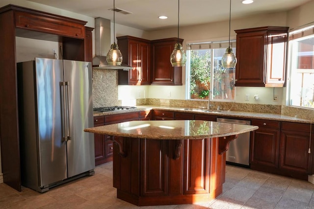 kitchen featuring sink, wall chimney exhaust hood, stainless steel appliances, pendant lighting, and a kitchen island