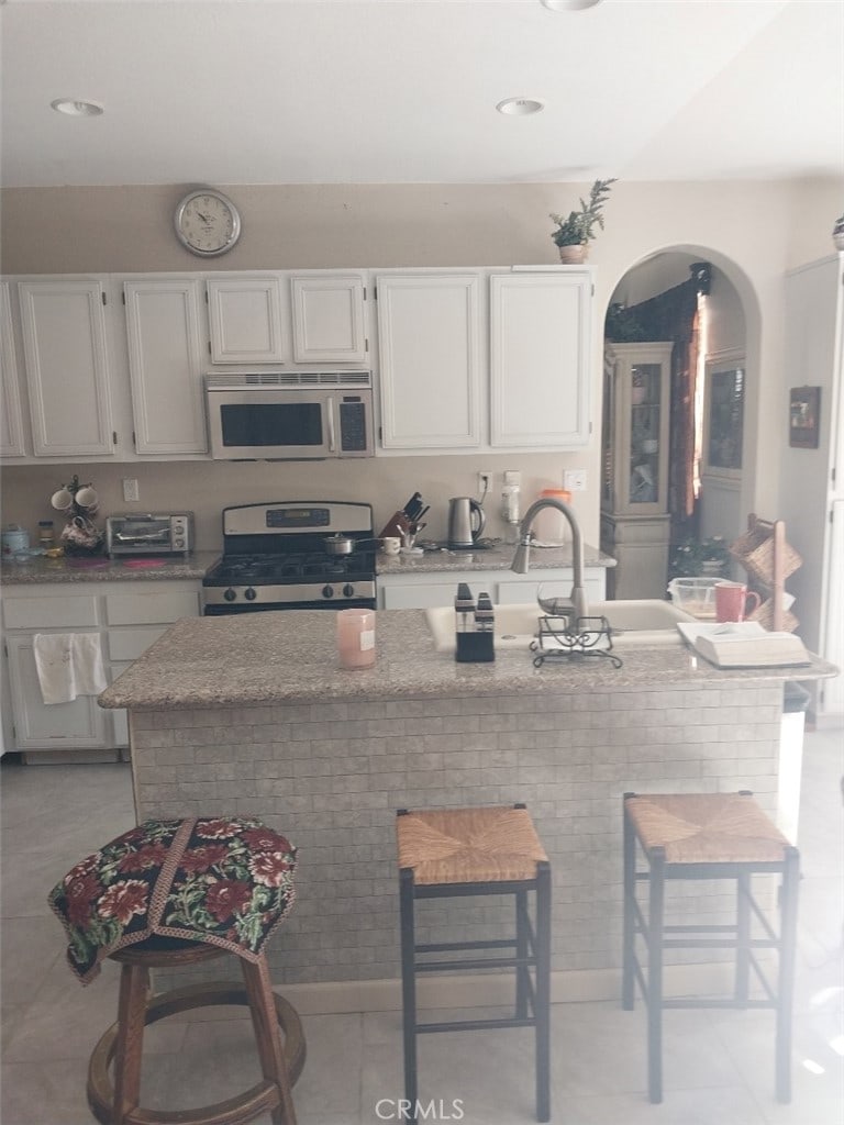 kitchen featuring a kitchen breakfast bar, stainless steel appliances, white cabinetry, and light stone counters