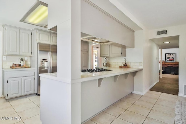 kitchen featuring gas cooktop, kitchen peninsula, light tile patterned floors, white cabinets, and stainless steel fridge with ice dispenser