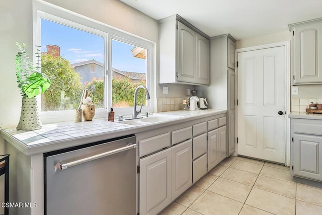 kitchen with tile countertops, sink, stainless steel dishwasher, gray cabinets, and light tile patterned flooring