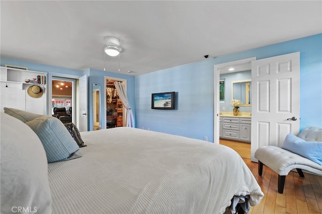 bedroom with ceiling fan, a walk in closet, light wood-type flooring, and connected bathroom