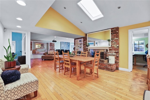 dining area featuring light wood-type flooring, a fireplace, and lofted ceiling with skylight