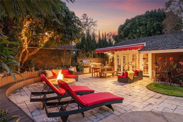 patio terrace at dusk featuring area for grilling, grilling area, french doors, and an outdoor living space with a fire pit