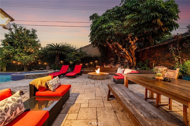 patio terrace at dusk with an in ground hot tub and an outdoor living space with a fire pit