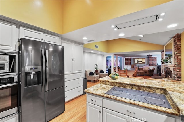 kitchen with refrigerator with ice dispenser, electric stovetop, stainless steel oven, lofted ceiling, and white cabinets