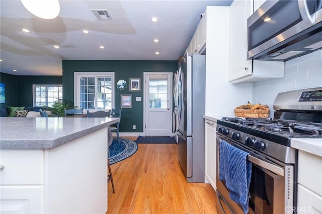 kitchen with backsplash, white cabinets, stainless steel appliances, and light hardwood / wood-style floors