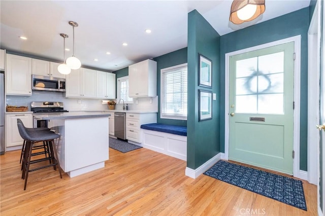 kitchen featuring a center island, appliances with stainless steel finishes, decorative light fixtures, light hardwood / wood-style floors, and white cabinetry