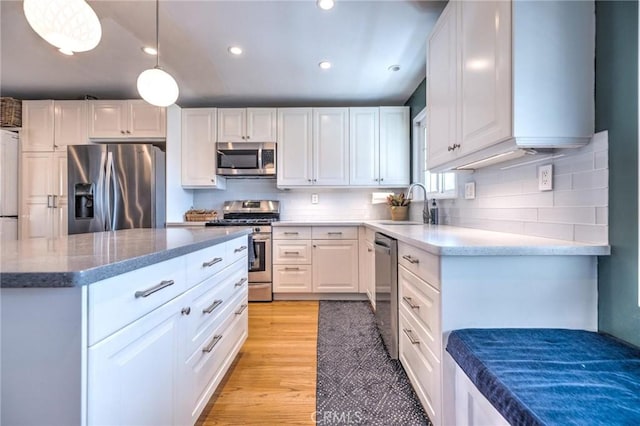 kitchen featuring pendant lighting, sink, light wood-type flooring, white cabinetry, and stainless steel appliances