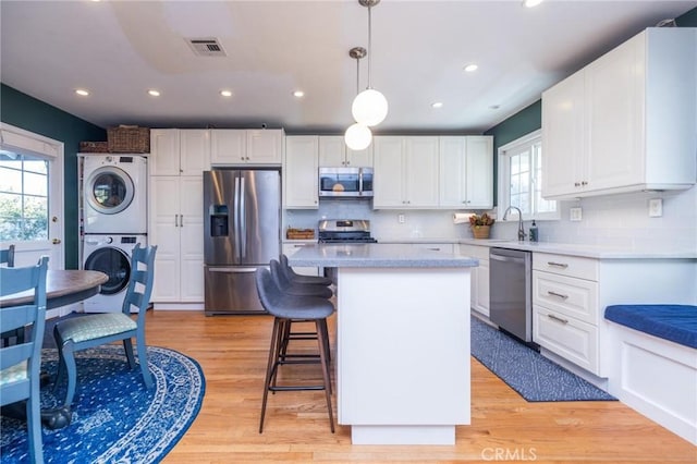 kitchen with light wood-type flooring, stainless steel appliances, decorative light fixtures, stacked washer and clothes dryer, and white cabinets