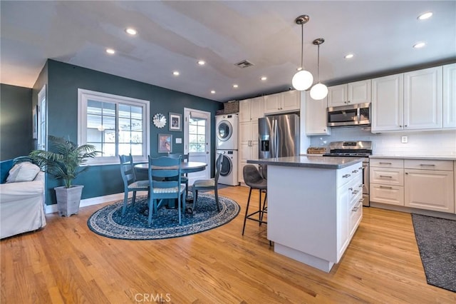 kitchen with appliances with stainless steel finishes, light wood-type flooring, stacked washer and dryer, and white cabinetry