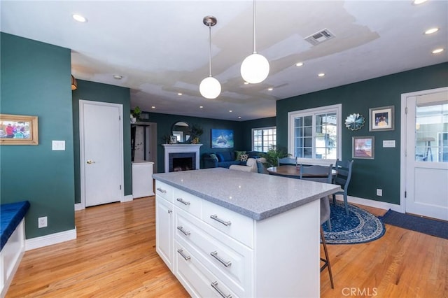 kitchen with light stone counters, pendant lighting, light hardwood / wood-style floors, a breakfast bar, and white cabinets