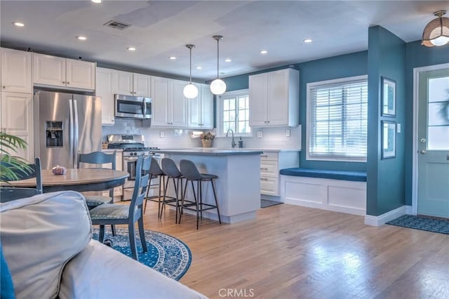 kitchen featuring stainless steel appliances, tasteful backsplash, light hardwood / wood-style flooring, pendant lighting, and white cabinets