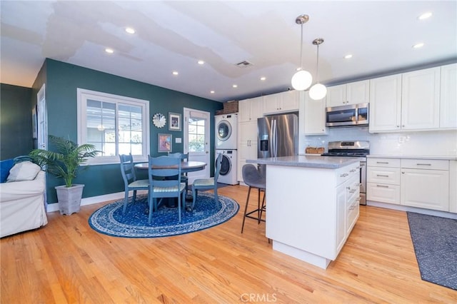 kitchen featuring white cabinetry, stacked washing maching and dryer, hanging light fixtures, stainless steel appliances, and light hardwood / wood-style flooring