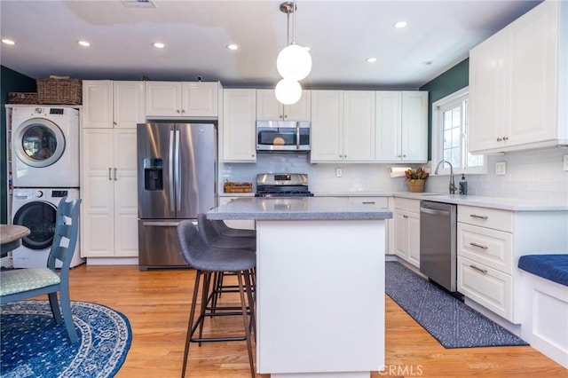 kitchen featuring white cabinets, pendant lighting, stainless steel appliances, and stacked washer / dryer