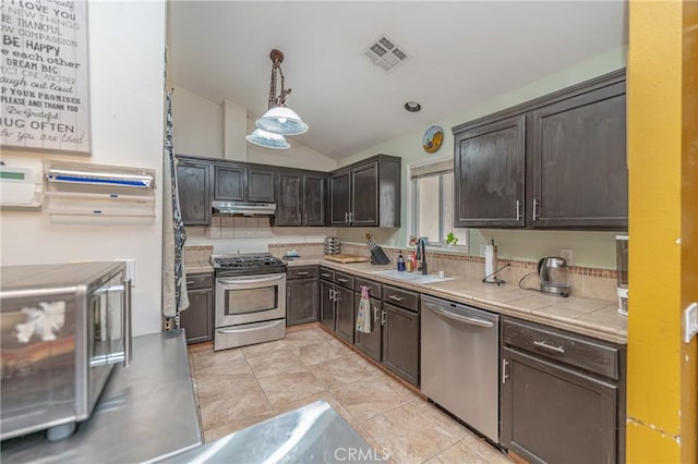 kitchen featuring appliances with stainless steel finishes, dark brown cabinetry, sink, decorative light fixtures, and lofted ceiling