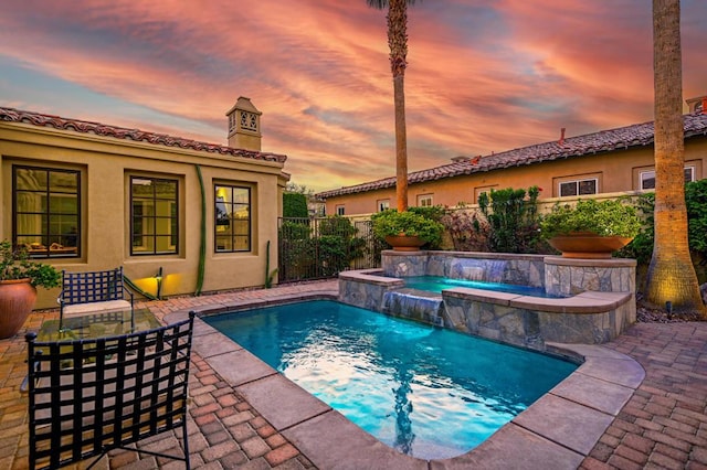 pool at dusk with an in ground hot tub, pool water feature, and a patio