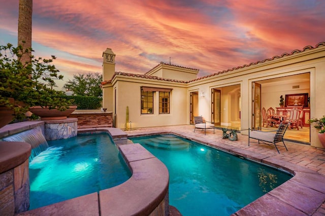 pool at dusk with pool water feature and a patio