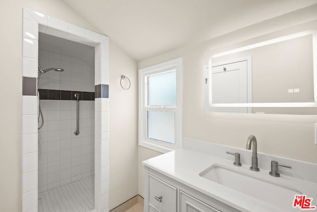 bathroom with tiled shower, vanity, and lofted ceiling