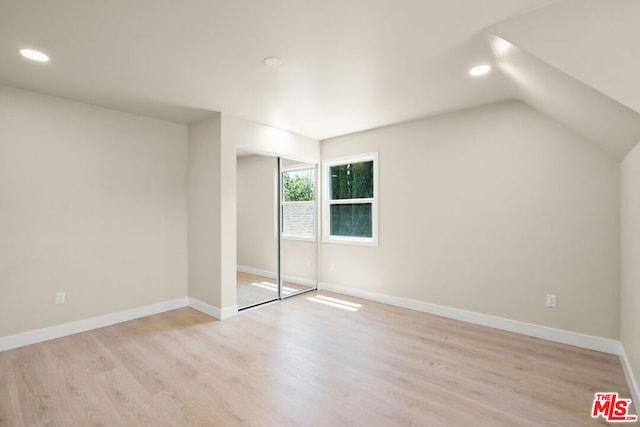 unfurnished bedroom featuring light hardwood / wood-style floors, a closet, and lofted ceiling