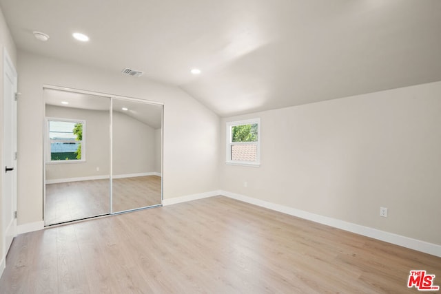 unfurnished bedroom featuring multiple windows, a closet, vaulted ceiling, and light wood-type flooring