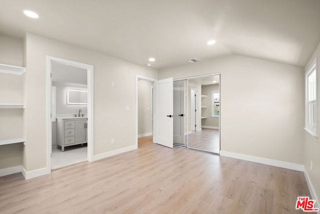 unfurnished bedroom featuring connected bathroom, sink, vaulted ceiling, and light wood-type flooring