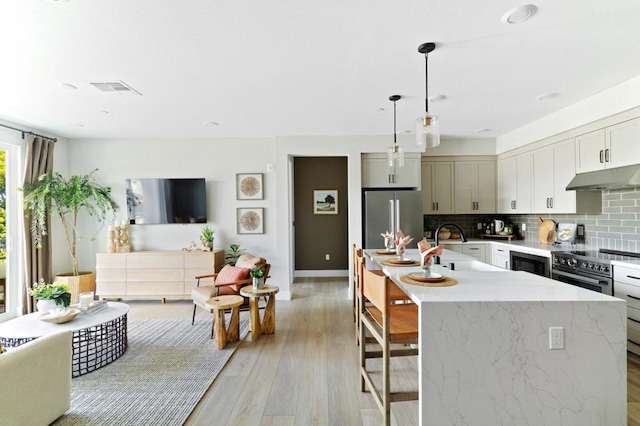 kitchen with backsplash, pendant lighting, sink, stainless steel refrigerator, and an island with sink