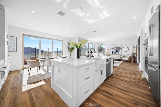 kitchen with a kitchen island with sink, dark wood-type flooring, white cabinets, and stainless steel appliances