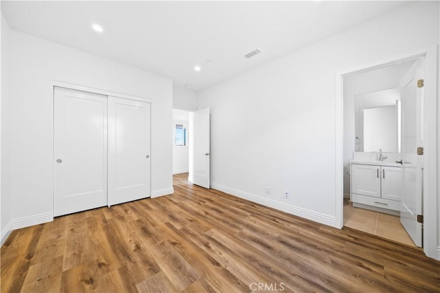 unfurnished bedroom featuring hardwood / wood-style flooring, ensuite bathroom, and a closet