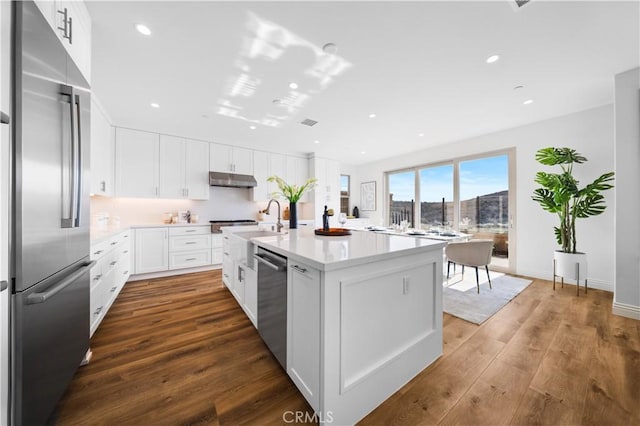 kitchen featuring sink, an island with sink, appliances with stainless steel finishes, dark hardwood / wood-style flooring, and white cabinetry