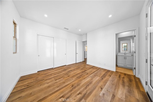 unfurnished bedroom with a closet, wood-type flooring, and ensuite bath