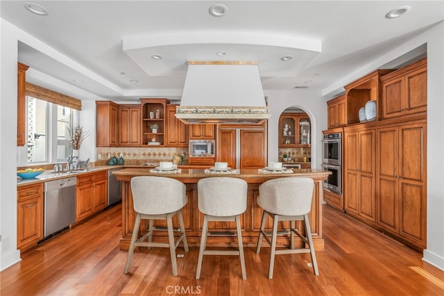 kitchen with decorative backsplash, built in appliances, hardwood / wood-style floors, a center island, and a breakfast bar area