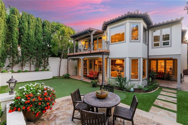 back house at dusk with a balcony and a patio